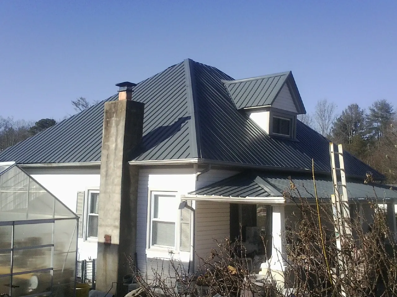 Dark blue standing seam metal roof on a white farmhouse with dormer — Slate & Tile Roof Repair by Roofing Brothers in Eastpointe