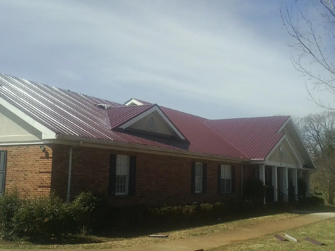 Red metal roof with gabled entries on a long brick building, from a Hail Damage Roof Repair job in Eastpointe