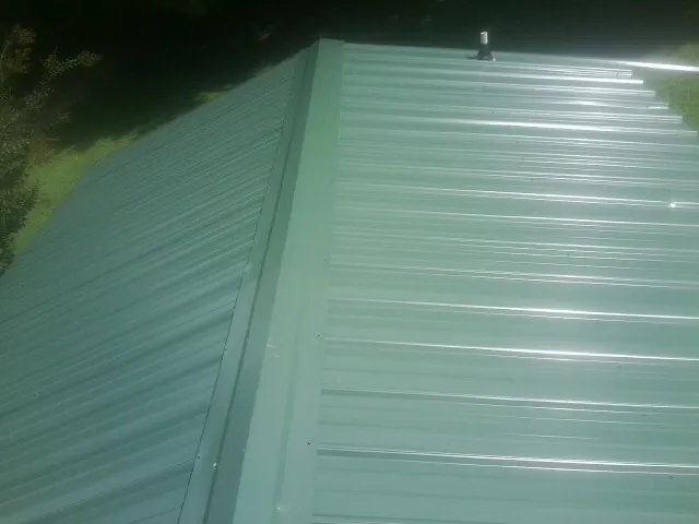 New green metal panels meeting at the ridge of a roof — Flat Roof Repair work by our crew in Eastpointe
