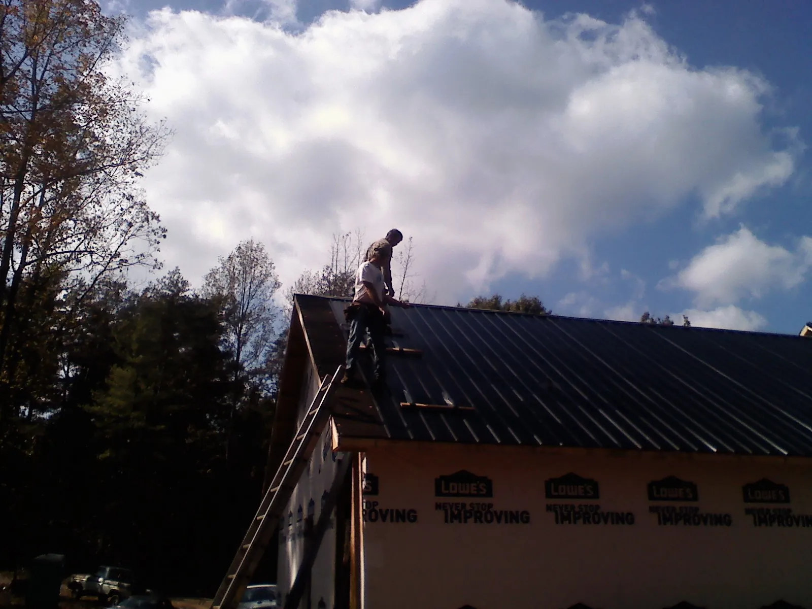 Roofer fastening dark metal panels high against a cloudy sky, from a Roof Inspection job in Eastpointe