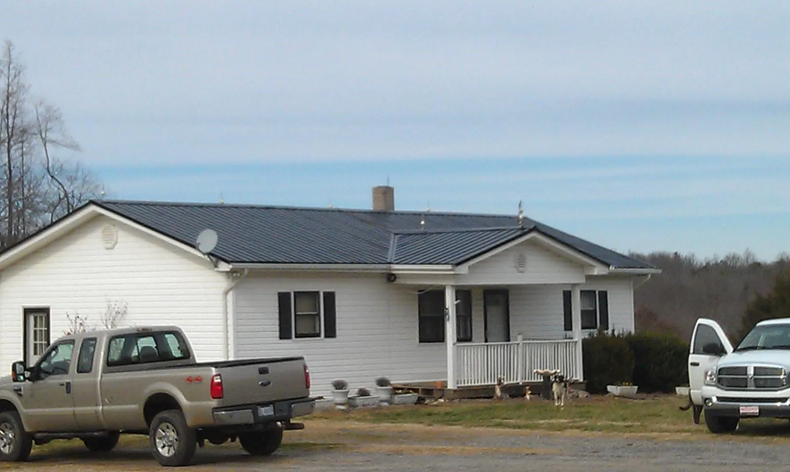 Finished dark metal roof on a white ranch home with work trucks parked in Eastpointe