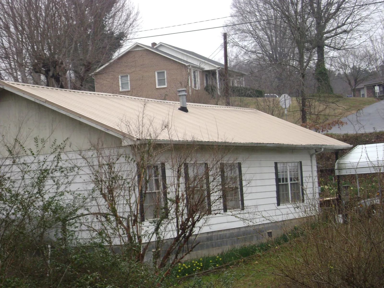 Tan metal roof on a white sided house set into a hillside — Commercial Roofing by Roofing Brothers in Eastpointe